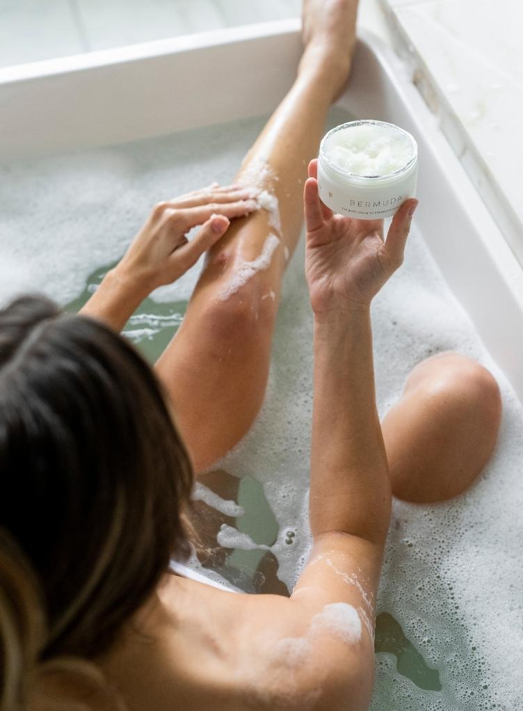 A woman in a bath holding a jar of Bushbalm scrub