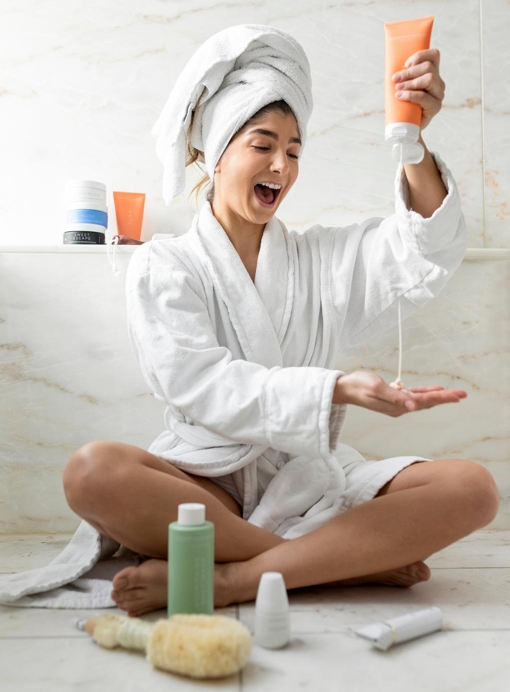 A woman in a robe and hair towel holding Bushbalm products